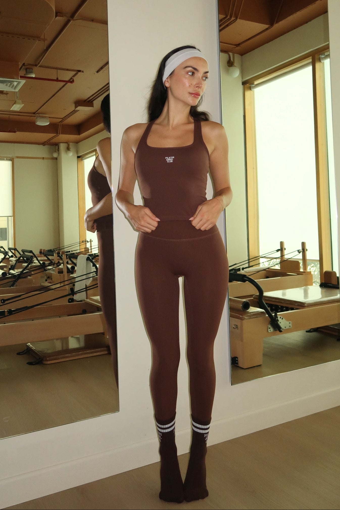 Person in a brown outfit standing in a Pilates studio.